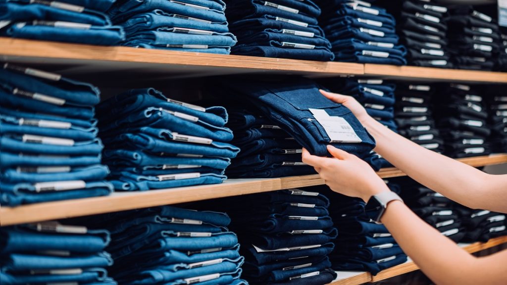 Cropped Shot Of Woman's Hand Selecting A Pair Of Trousers From The Display Shelf While Shopping In A Clothing Store In The City